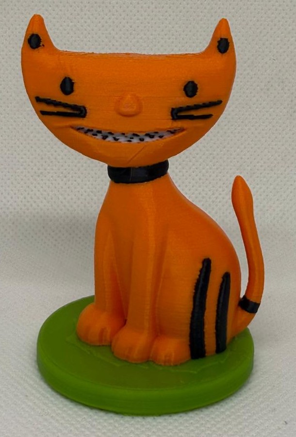 Finished 3D print of a grinning orange cat with sharp teeth sitting on grass